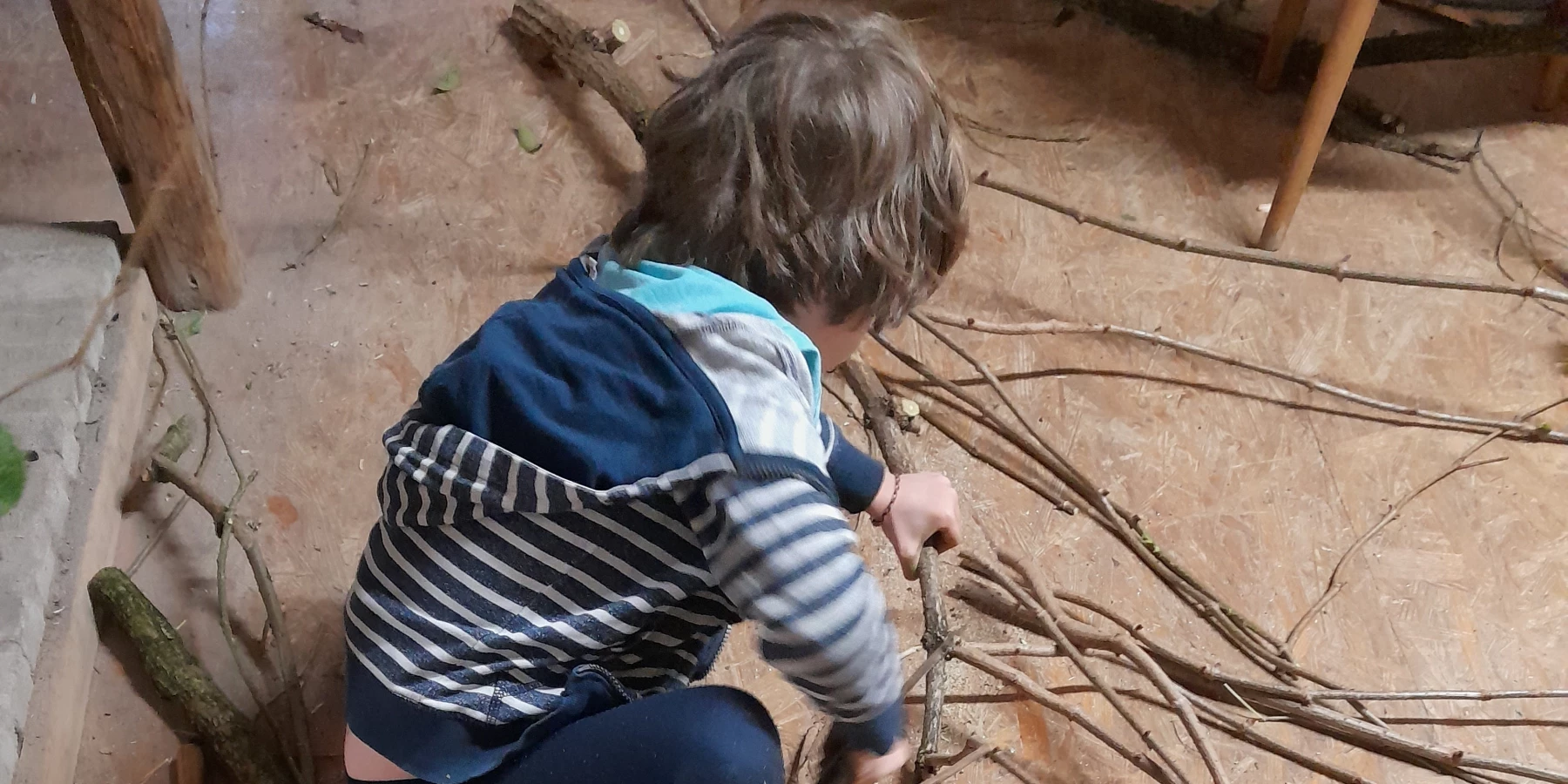 Foto von einem kleinen Kind das an einem Bündel von Zweigen sägt