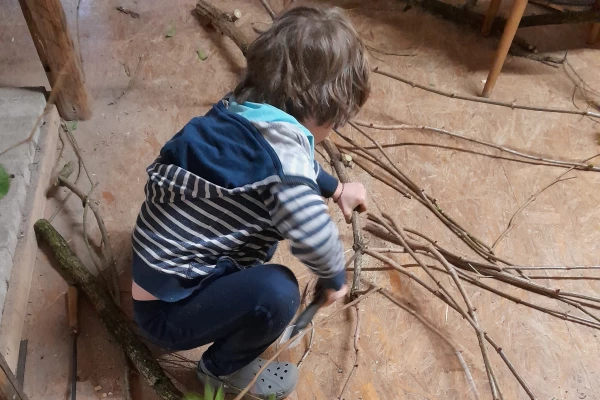 Foto von einem kleinen Kind das an einem Bündel von Zweigen sägt