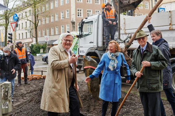 Drei Menschen im Vordergrund mit einer Schaufel. Im Hintergrund ein Bagger und Menschen in Arbeitskleidung