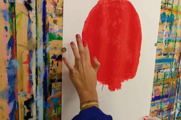 Eine weibliche Hand mit roten Fingernägeln macht finger painting in Form eines großen Kreises mit roter Farbe