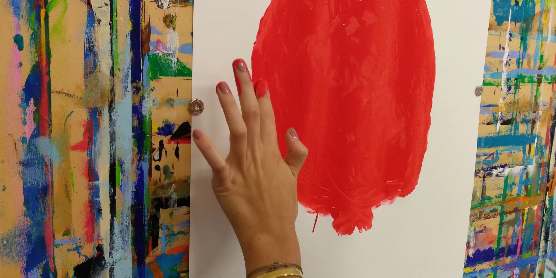 Eine weibliche Hand mit roten Fingernägeln macht finger painting in Form eines großen Kreises mit roter Farbe