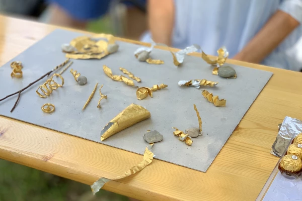 Auf einem Tisch liegen goldene, handgemachte Objekte, die zuerst wie Schmuck aussehen aber abstrakter sind