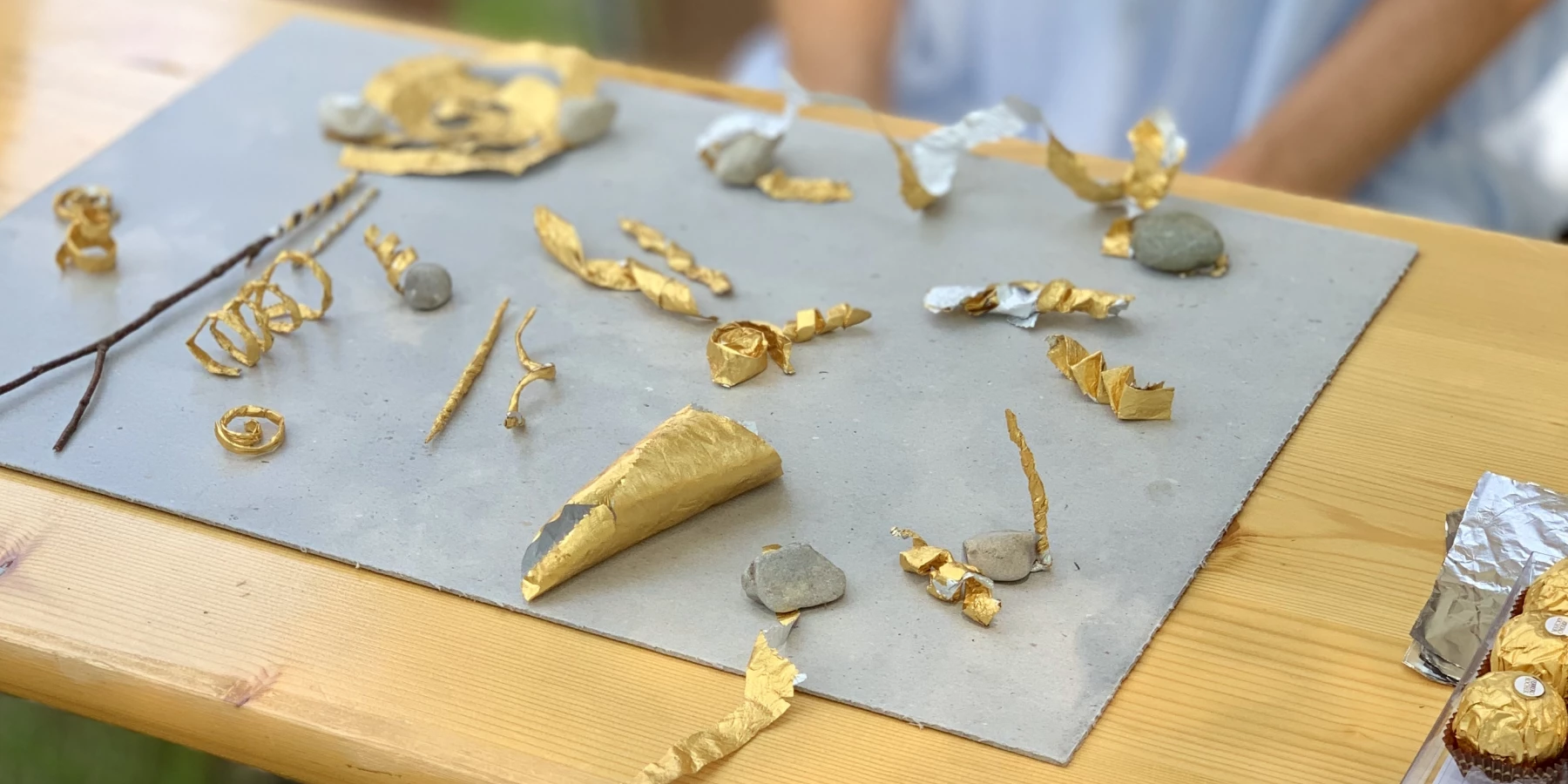 Auf einem Tisch liegen goldene, handgemachte Objekte, die zuerst wie Schmuck aussehen aber abstrakter sind