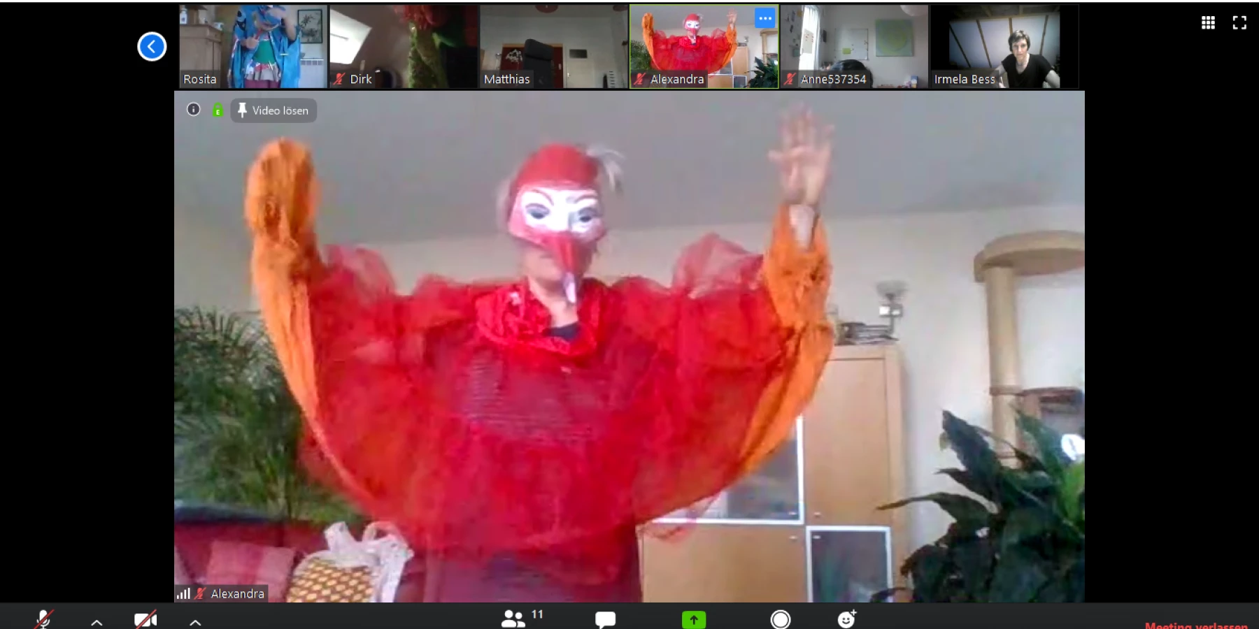 Gruppen Videocall Screenshot mit einer rot gekleideten Figur in der Mitte mit Schnabelmaske, die die Arme flügelartig ausbreitet