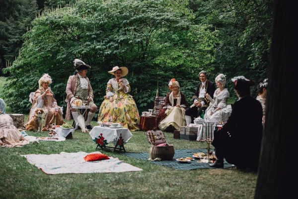 Damen und Herren in Rokokokostümen sitzen beim Picknick im Park
