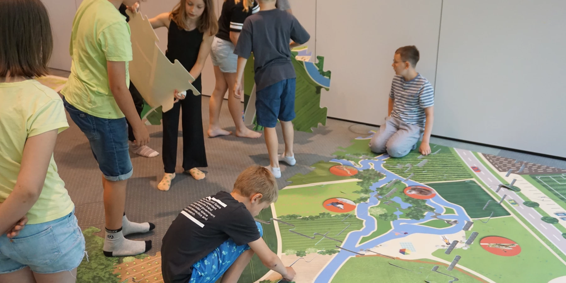 Kinder spielen auf einem Teppich, auf dem eine Landkarte mit Fluss gedruckt ist.