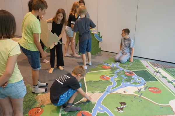 Kinder spielen auf einem Teppich, auf dem eine Landkarte mit Fluss gedruckt ist.