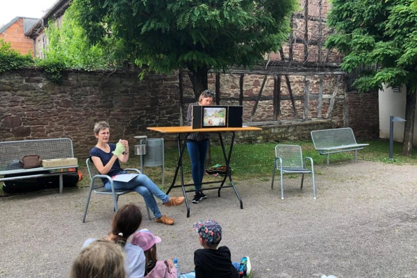 Eine Frau liest im Westtaschenpark ein Buch vor, während Kinder zuhören