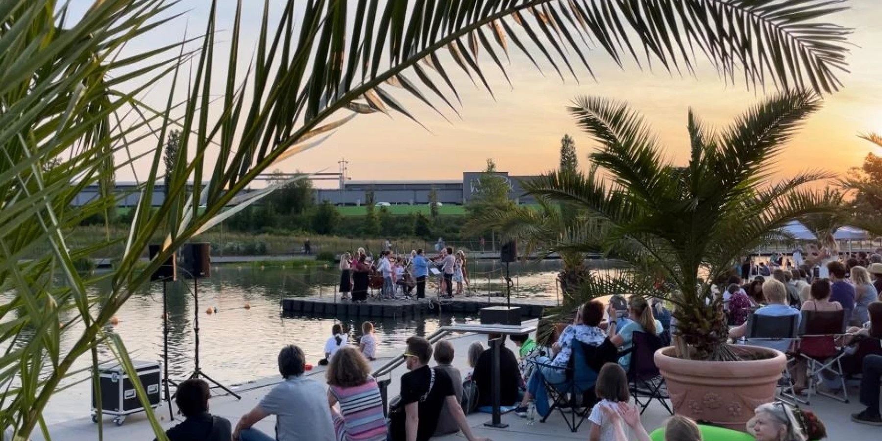 Menschen sitzen an einem Fluss bei Sonnenaufgang umgeben von Palmen in Töpfen