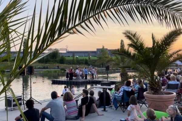 Menschen sitzen an einem Fluss bei Sonnenaufgang umgeben von Palmen in Töpfen