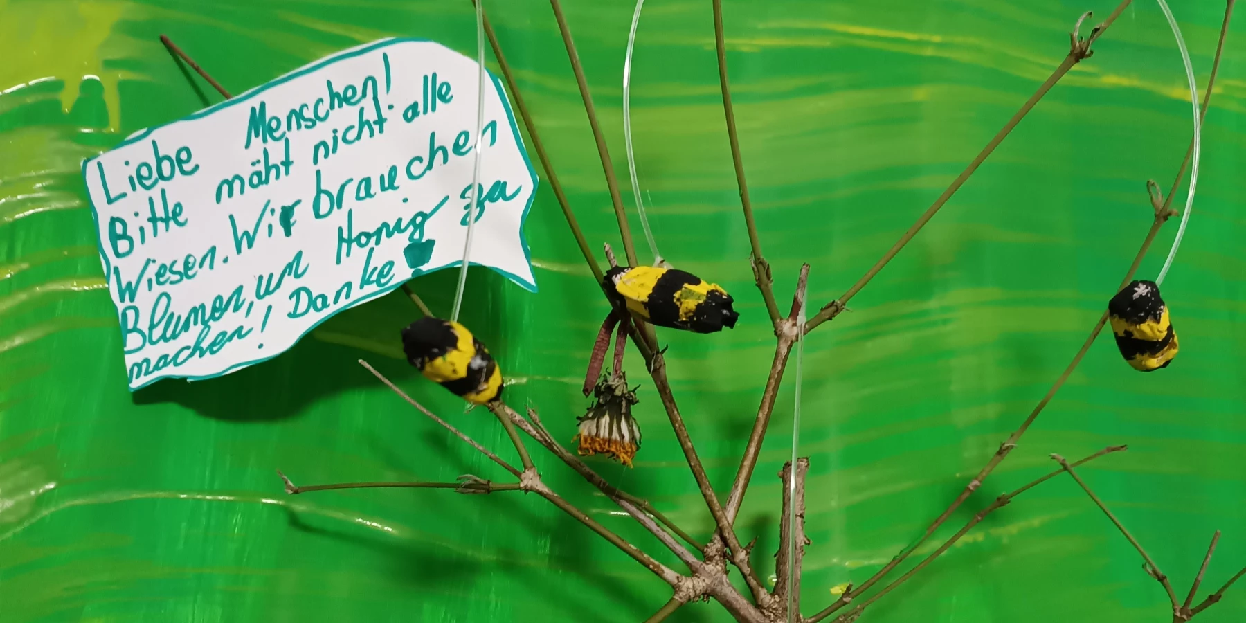 An einem verzweigten Ast hängen selbstgebastelte Bienen und eine Sprechblase
