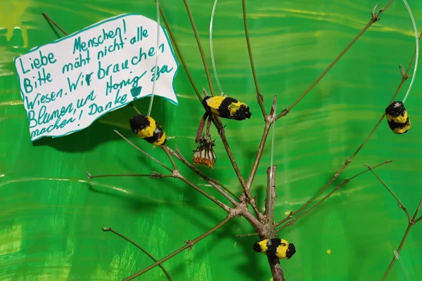 An einem verzweigten Ast hängen selbstgebastelte Bienen und eine Sprechblase