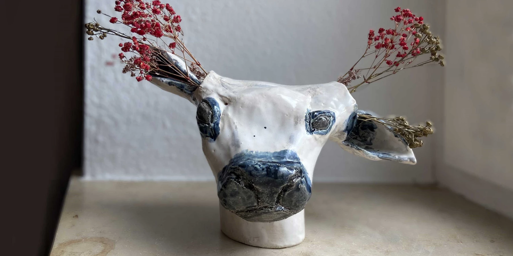 Der Kopf einer Kuh aus Keramik, mit getrockneten Blumen die aus ihren Ohren kommen