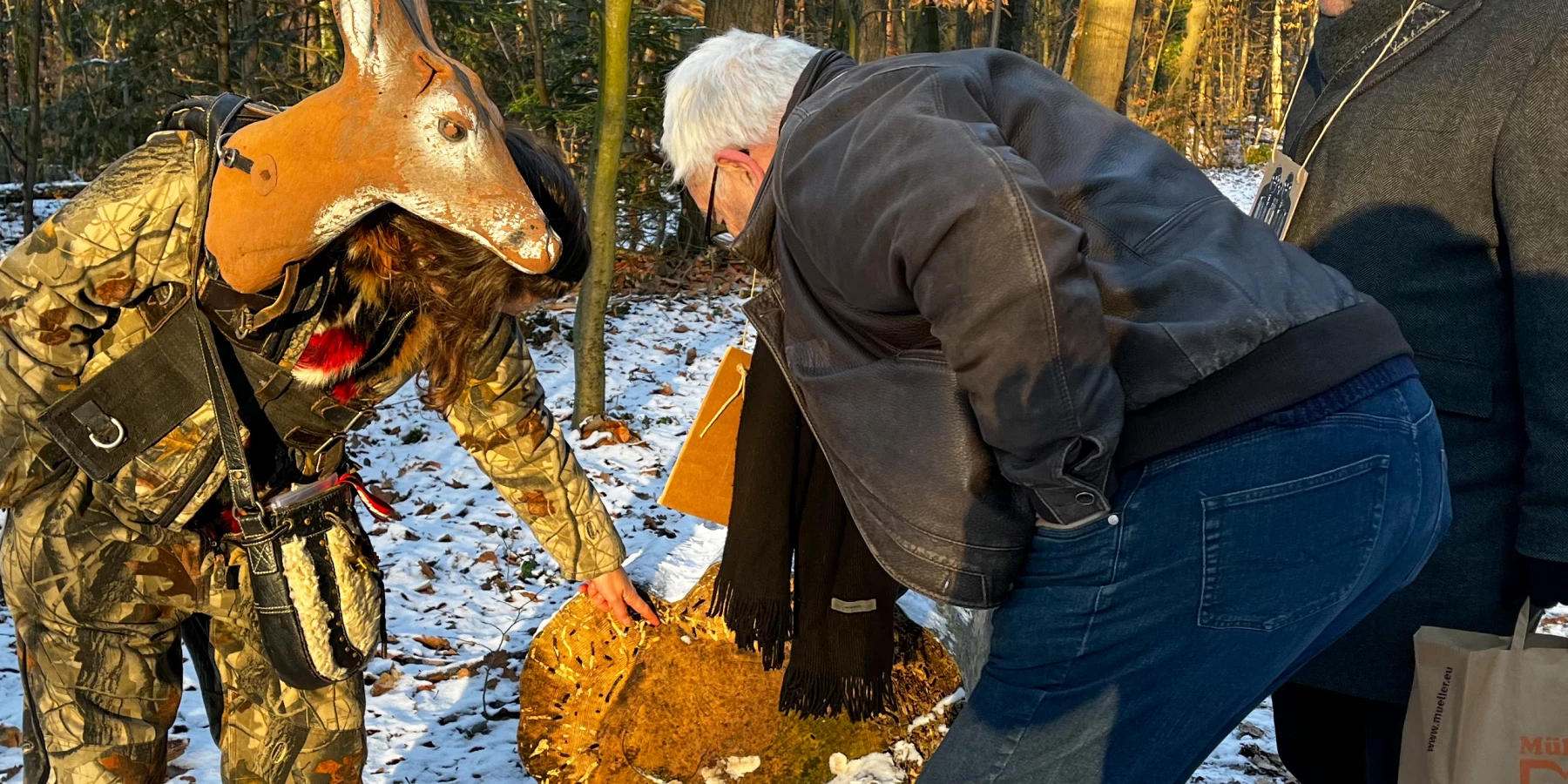 Eine Frau mit Rehkopf und ein Mann beugen sich über etwas im Schnee
