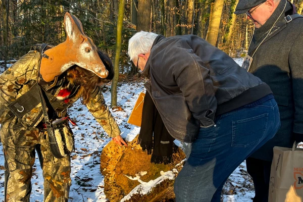 Eine Frau mit Rehkopf und ein Mann beugen sich über etwas im Schnee