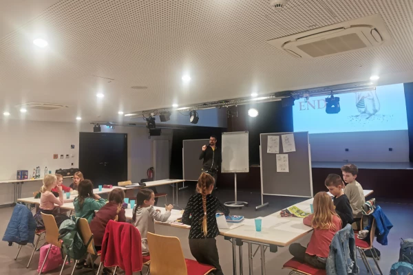 Kinder sitzen an Tischen, während ein Mann eine Präsentation hält