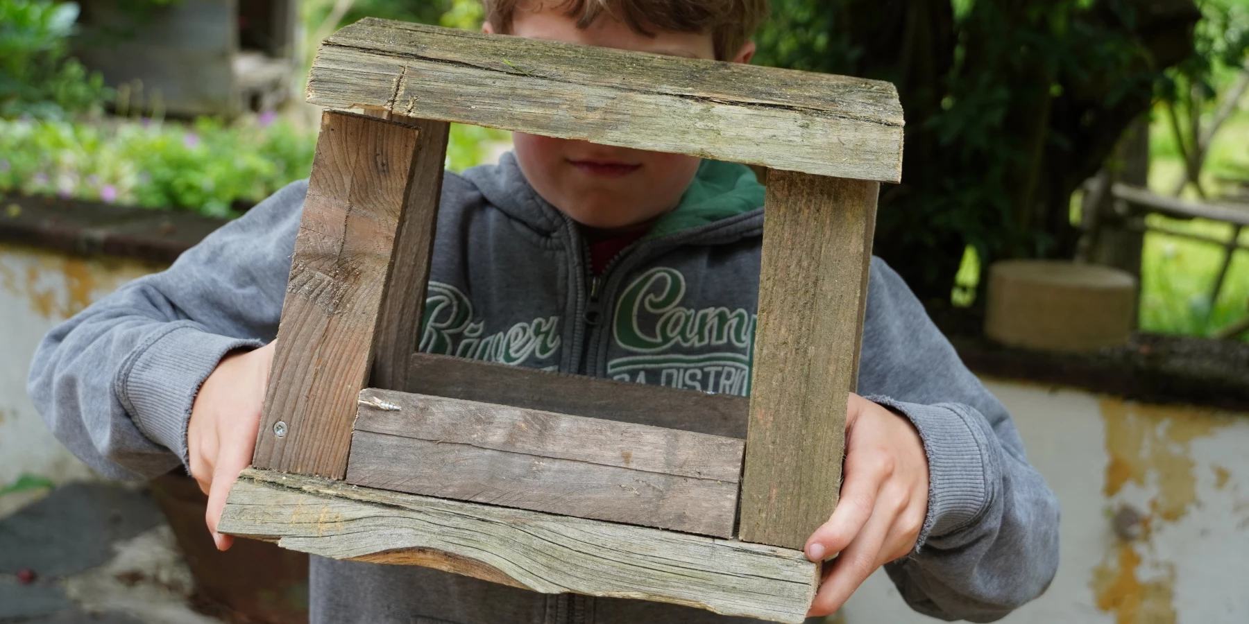 Ein Junge hält eine aus Holz gebaute Futterstelle für Vögel hoch