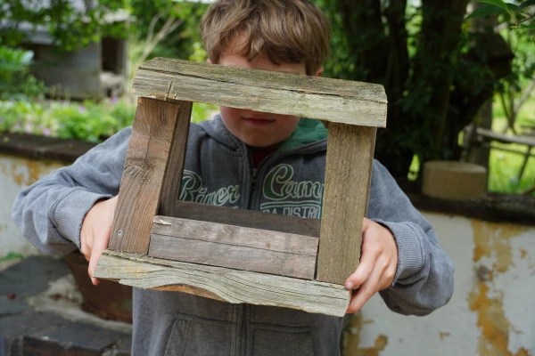 Ein Junge hält eine aus Holz gebaute Futterstelle für Vögel hoch