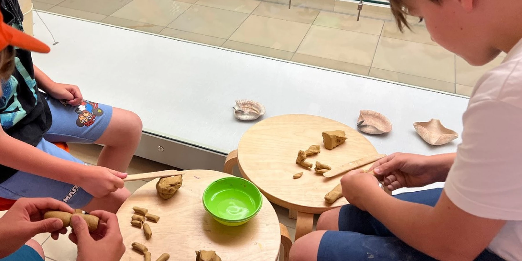 Kinder arbeiten mit Ton vor einer Vitrine mit Gefäßen alter Kulturen