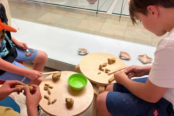 Kinder arbeiten mit Ton vor einer Vitrine mit Gefäßen alter Kulturen