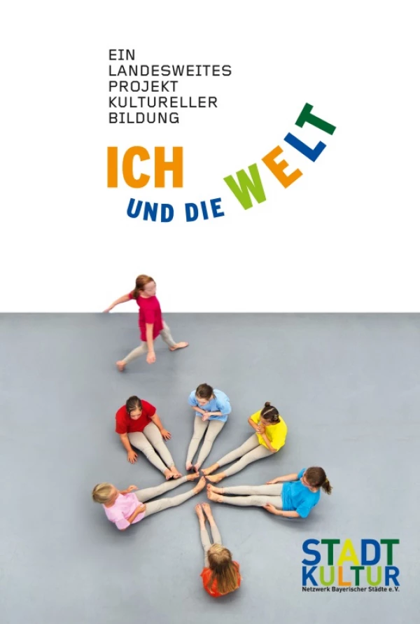 Titelseite „ICH und die WELT“: Kinder bei Tanzperformance mit ausgestreckten Beinen im Kreis, eine Figur geht um sie herum
