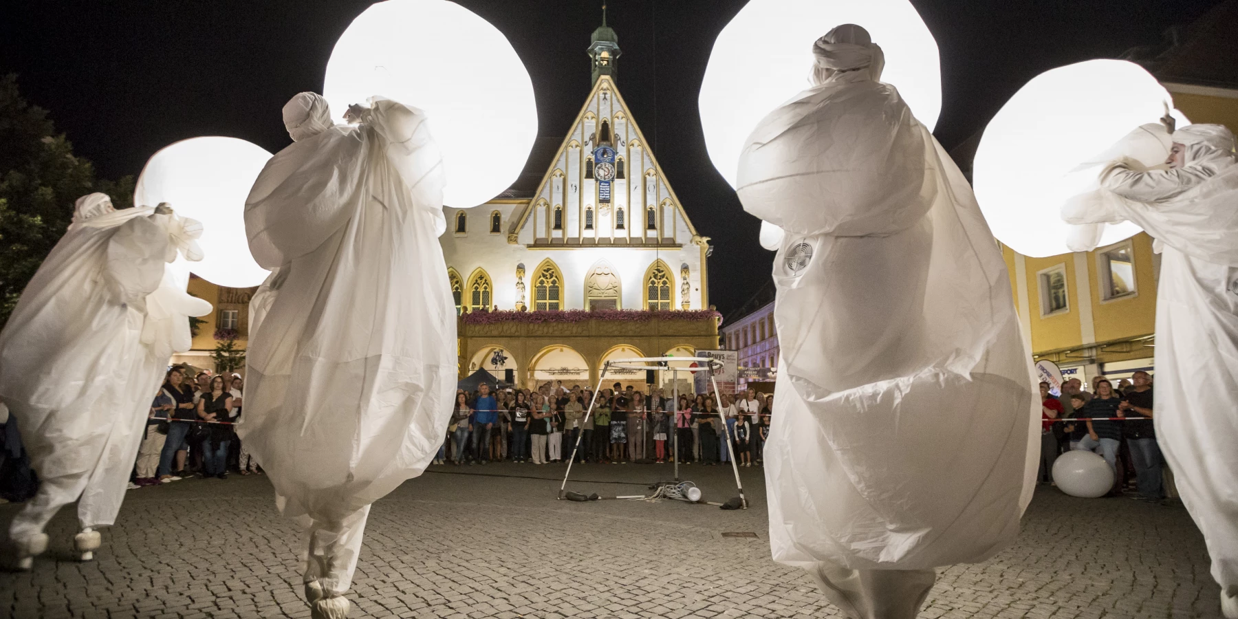 Es ist eine Nachtveranstaltung und die Performer hantieren in weißen Kostümen mit grell weiß leuchtenden Objekten.