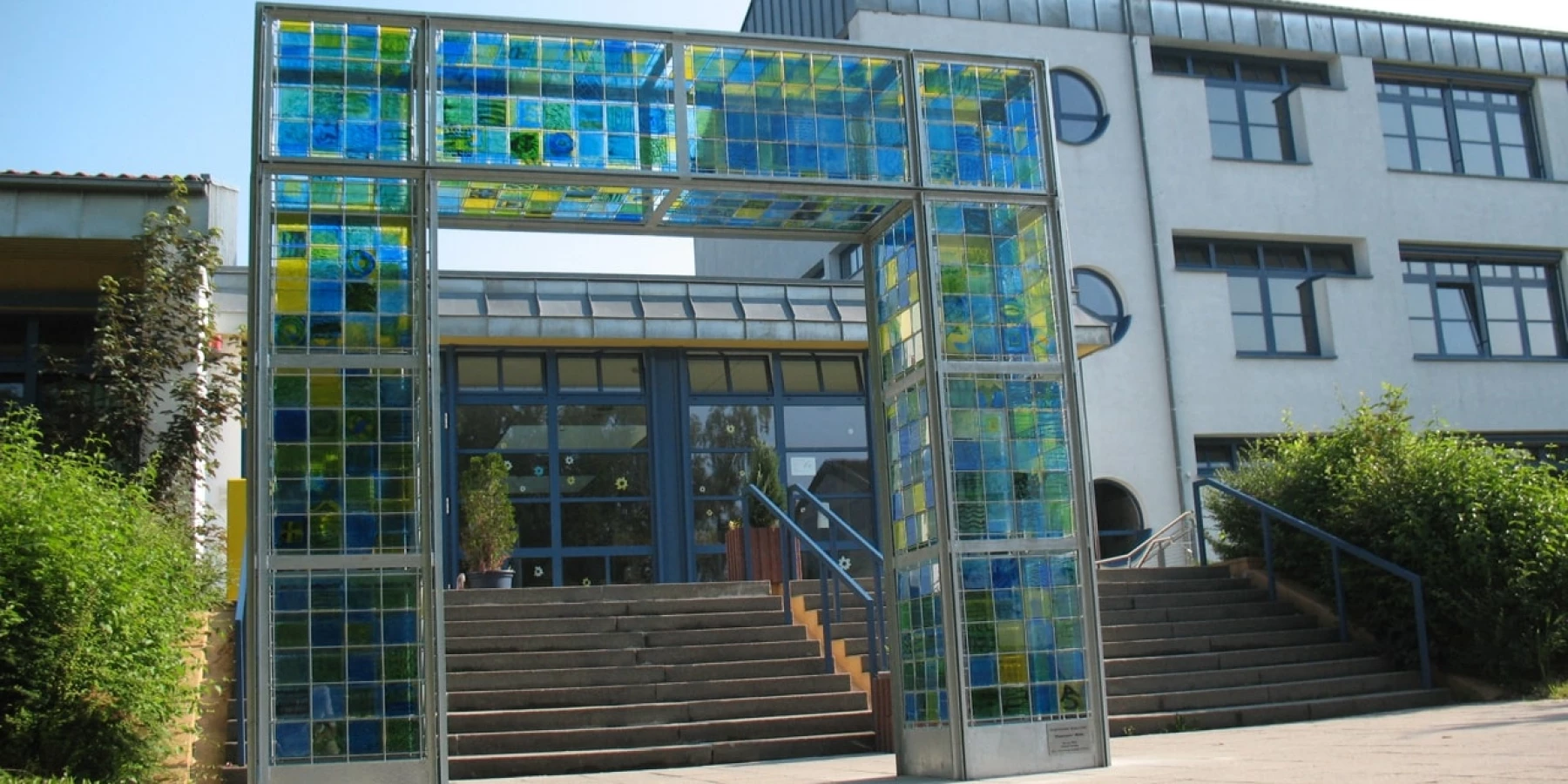 Ein großes Tor vor einem Gebäude, gebaut aus gelben, grünen und blauen Glasfliesen.
