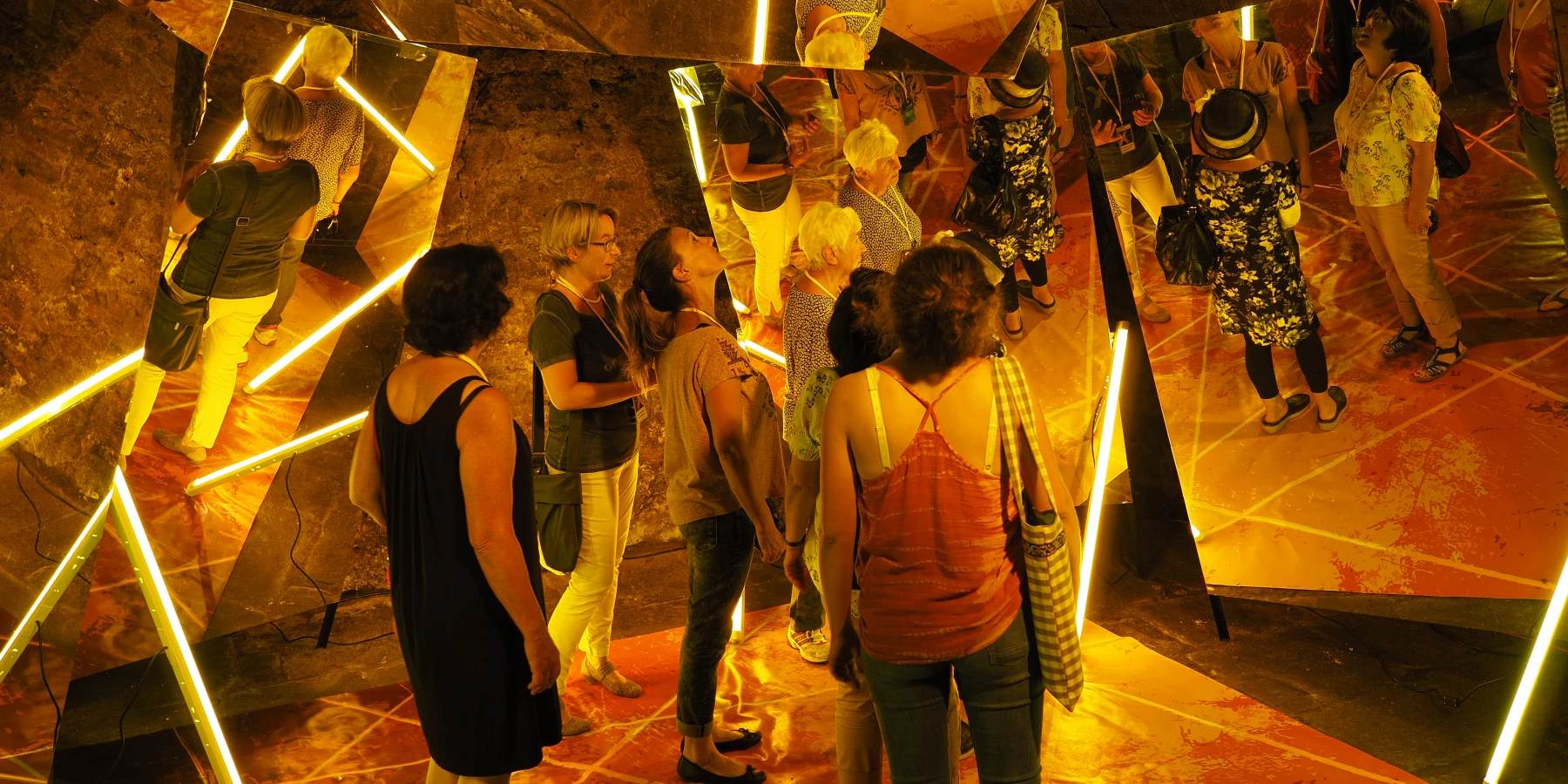 Eine Gruppe Erwachsener steht inmitten einer Installation von Spiegeln, Neonröhren und goldener Bodenfolie