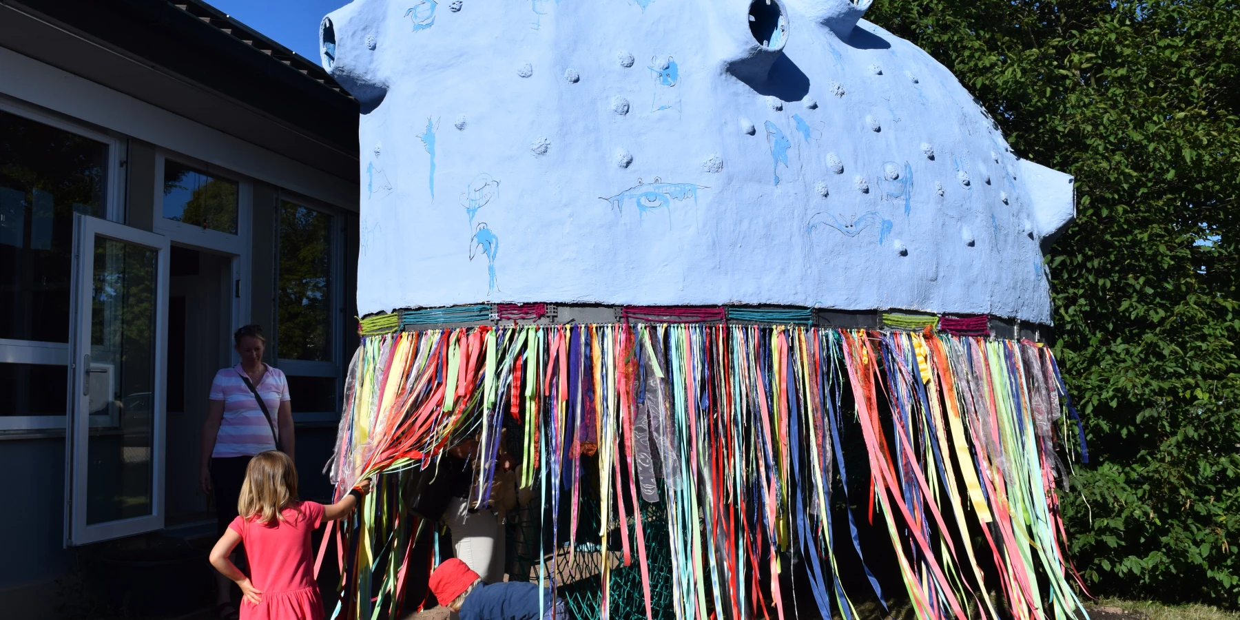 Eine große bunte Skulptur steht draußen vor einem Gebäude und Kinder spielen damit.